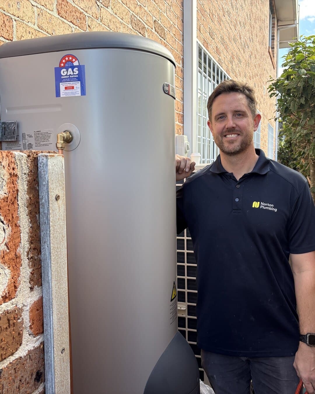 Adam Norton beside a newly installed Rheem hot water system, Norton Plumbing Eastern Suburbs