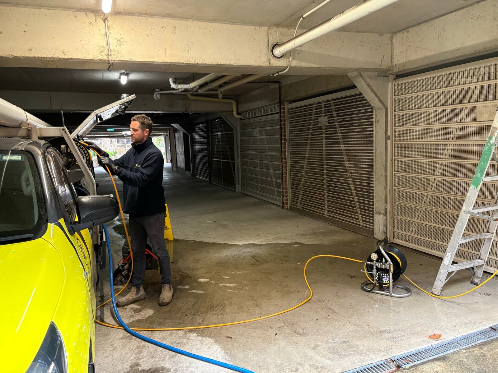Adam Norton setting up high-pressure jetting equipment in the underground car park of a Rose Bay apartment building, beside the yellow Norton Plumbing truck