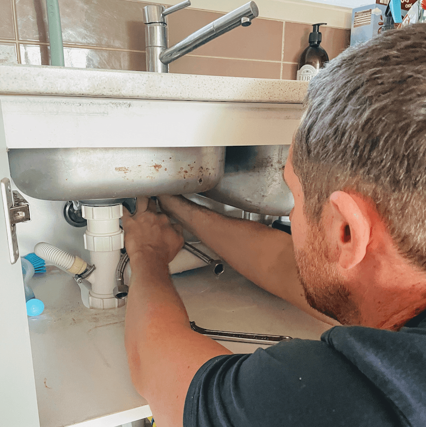 Adam using acoustic leak detection equipment under a sink to locate a hidden pipe leak