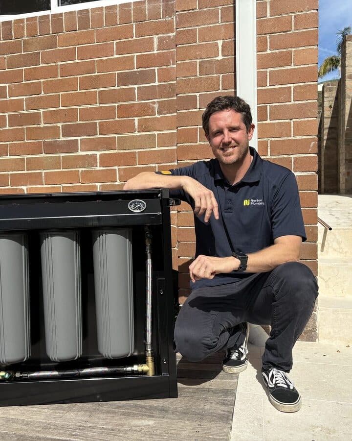 Adam from Norton Plumbing beside a Puretec FilterWall with the cover off, showing the three filter cartridges, at a Randwick home