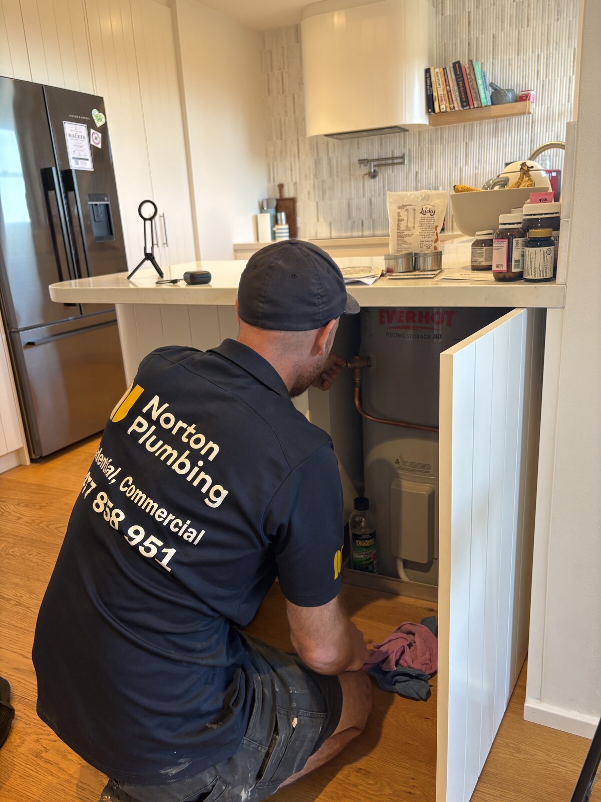 Adam Norton of Norton Plumbing working on the relief valve of an Everhot electric storage hot water tank built into a kitchen island cupboard at a Coogee home