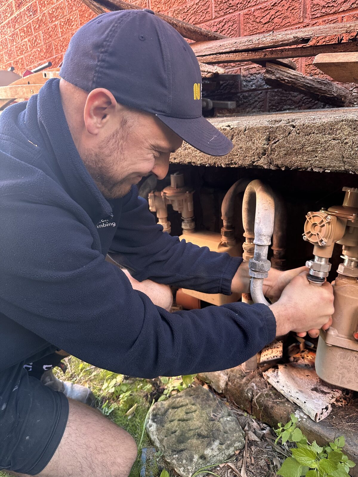 Greg from Norton Plumbing fitting a new gas regulator into the pipework under a Rose Bay home