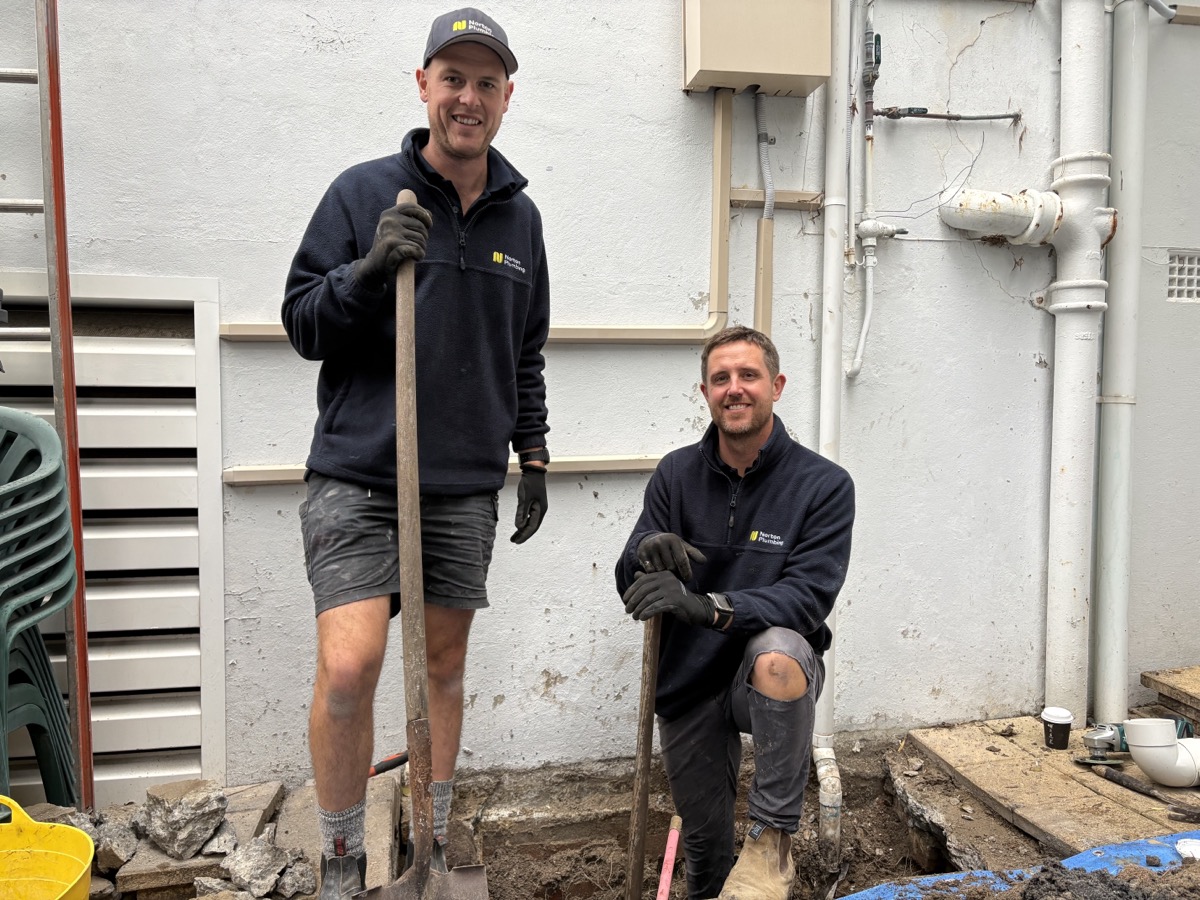 Greg and Adam from Norton Plumbing standing in the excavation trench at Mount Street Coogee, shovels in hand, blue protective sheeting on the ground