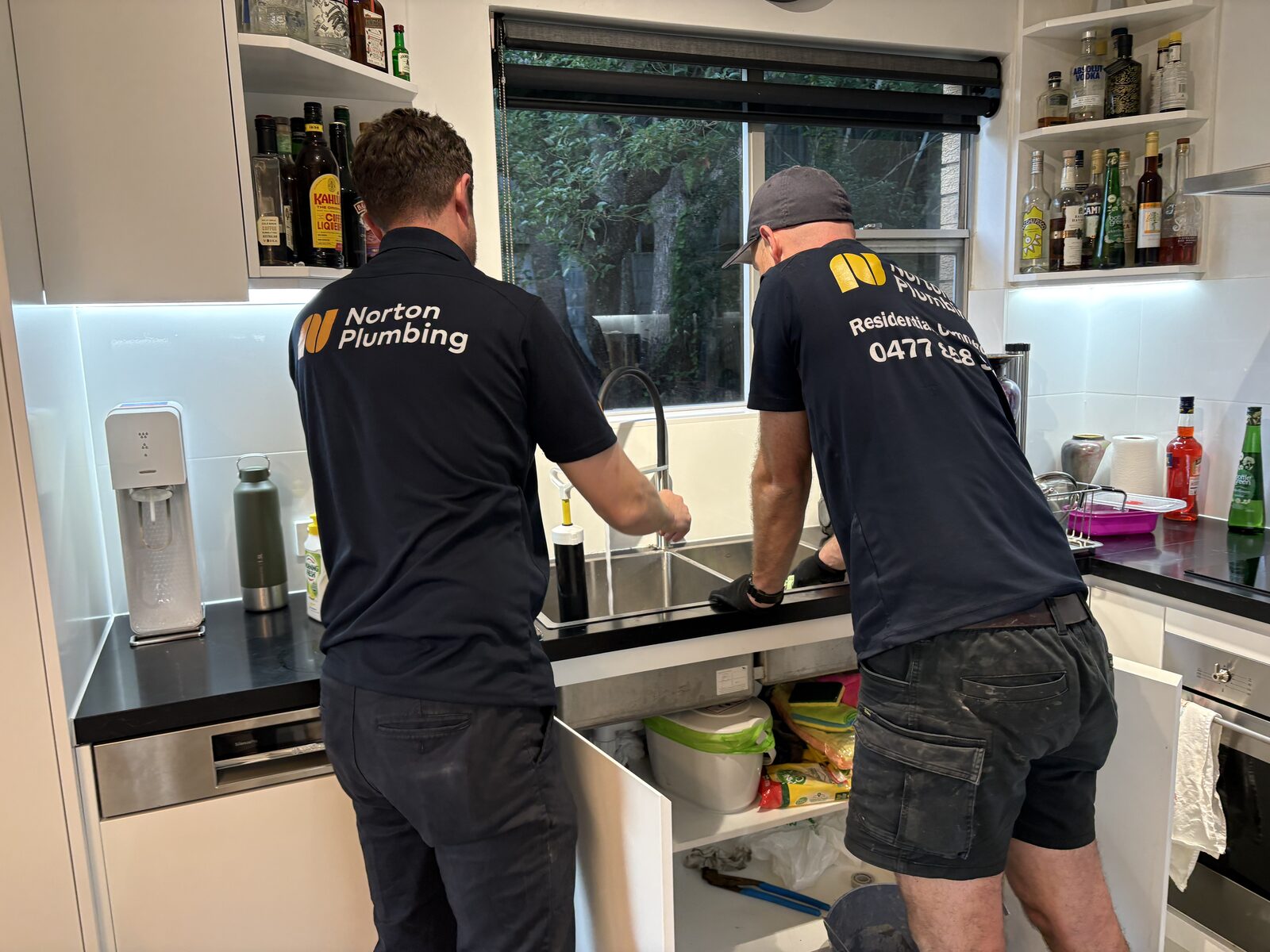 Adam and Greg from Norton Plumbing at a Coogee kitchen sink, running the tap to test the drain after clearing the blocked kitchen line