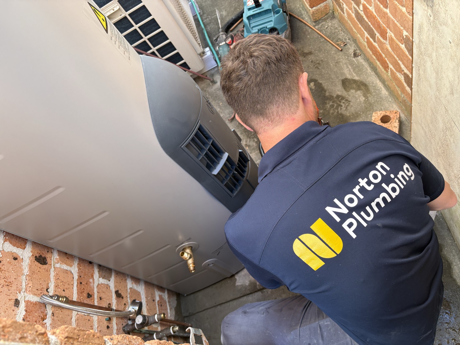 Adam Norton from Norton Plumbing in a branded polo connecting the copper fittings on a new Rheem gas hot water system in Maroubra