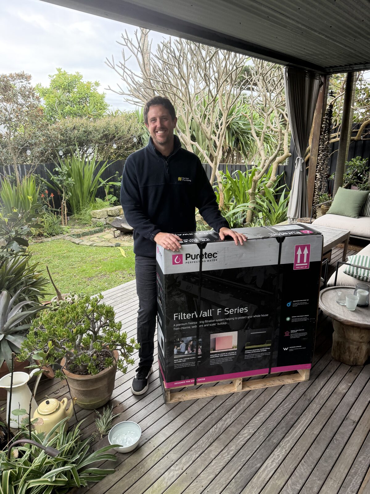 Adam Norton from Norton Plumbing standing with a boxed Puretec FilterWall F Series whole-house water filter on the back deck of a North Bondi home