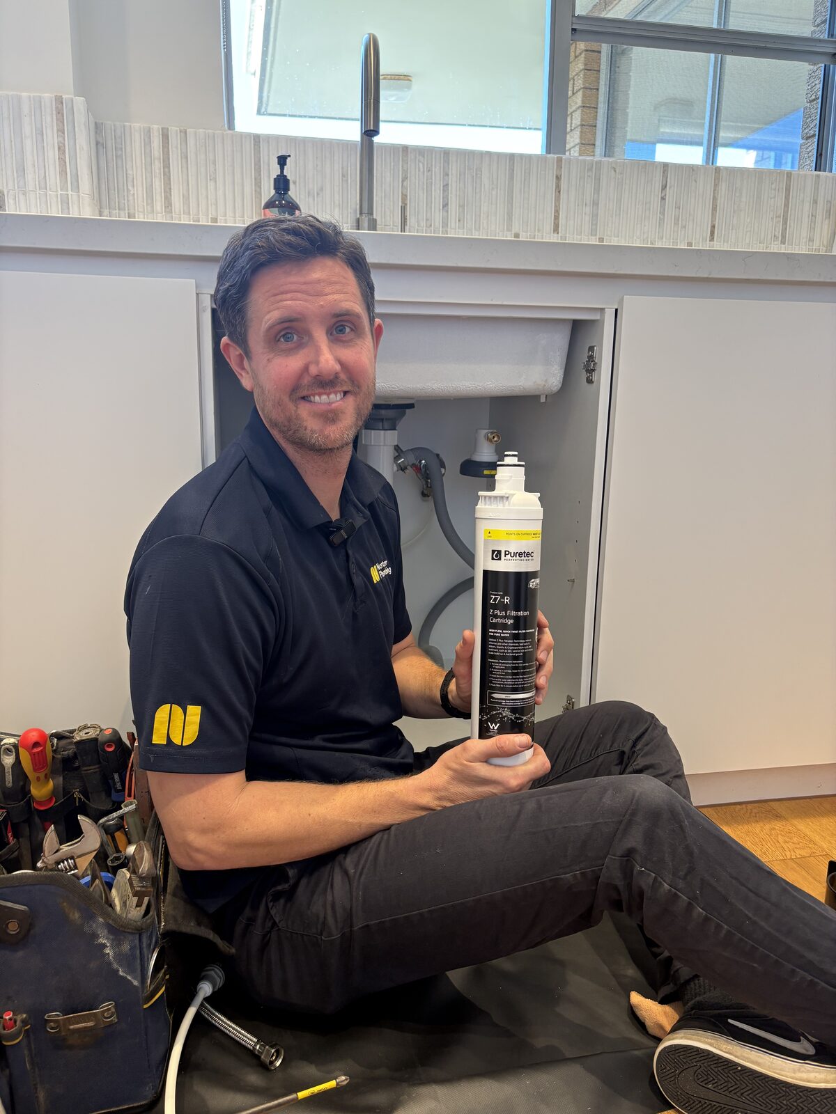 Adam Norton from Norton Plumbing holding a Puretec Z7-R filtration cartridge beside the open sink cupboard of a Coogee kitchen before fitting the under-sink water filter