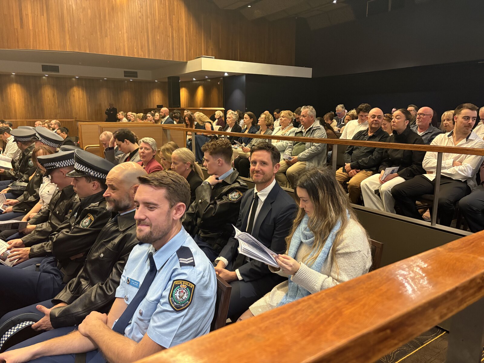 Adam and Rebecca Norton seated in the audience at the NSW Police Medals and Awards Presentation Day, surrounded by North Shore and Northern Beaches Police officers