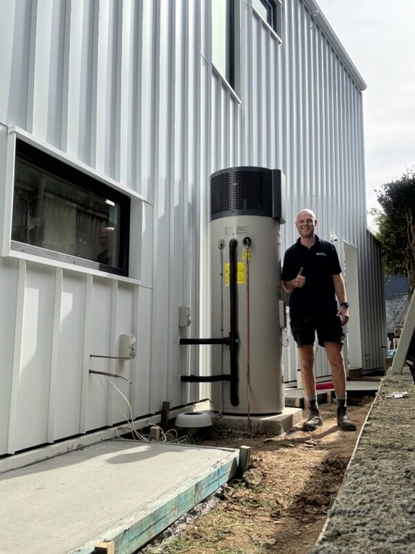 Adam Norton from Norton Plumbing standing beside a completed Rinnai Enviroflo heat pump hot water system at a Maroubra home