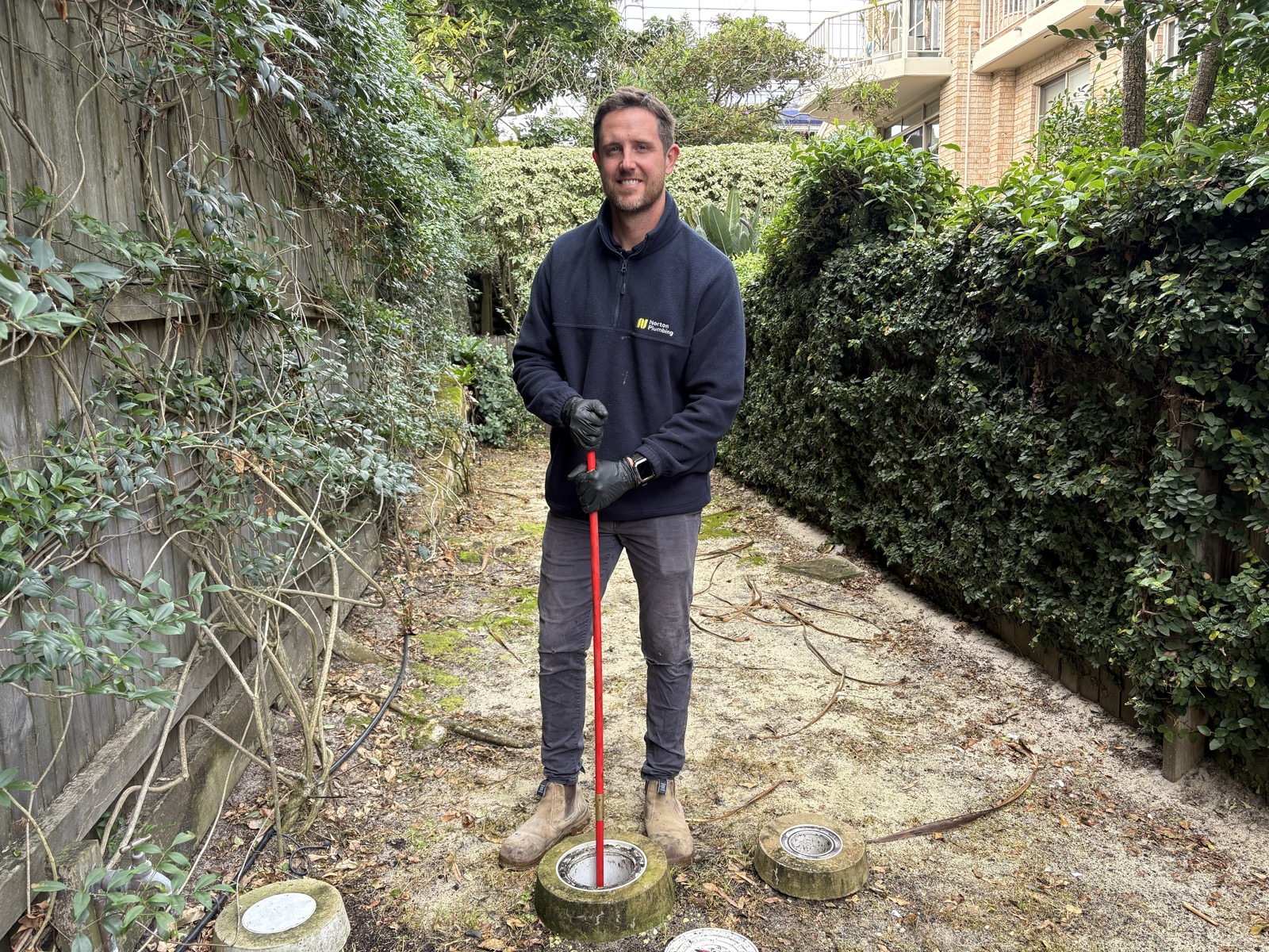 Adam Norton standing at open drain inspection chambers in the garden of a Rose Bay apartment block, June 2026