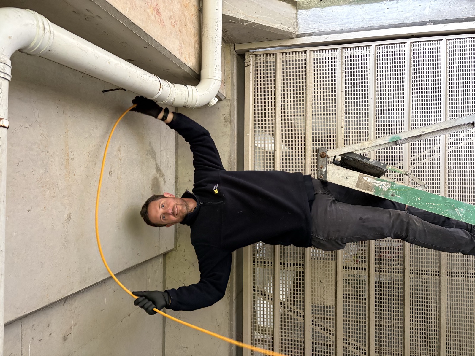 Adam Norton on a ladder on the exterior of a Rose Bay apartment building, feeding an electric eel into a high-level drain access point on the wall