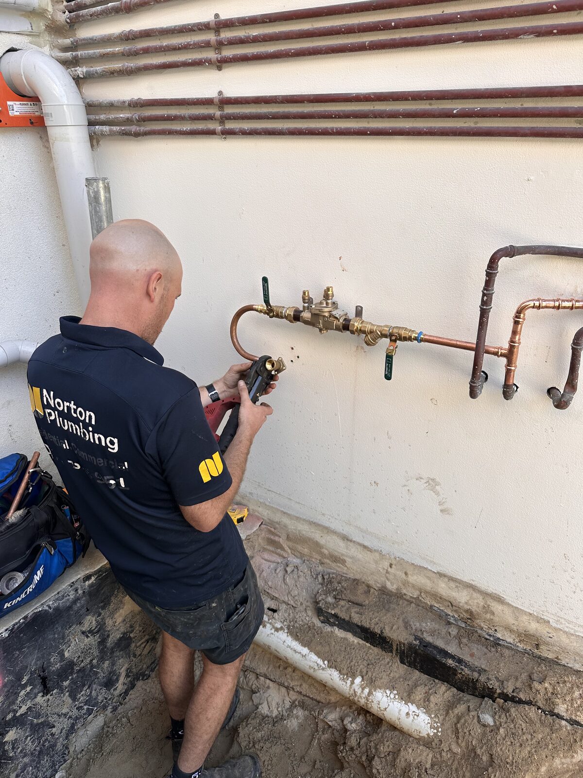 Adam Norton of Norton Plumbing installing a reduced pressure zone backflow prevention device on the external wall of a Bondi strata apartment building