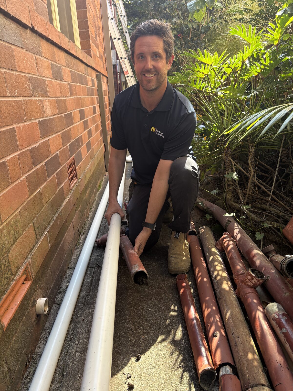 Adam Norton of Norton Plumbing kneeling beside the removed cast iron waste stack sections and the new PVC pipe at a Coogee Bay Road strata block