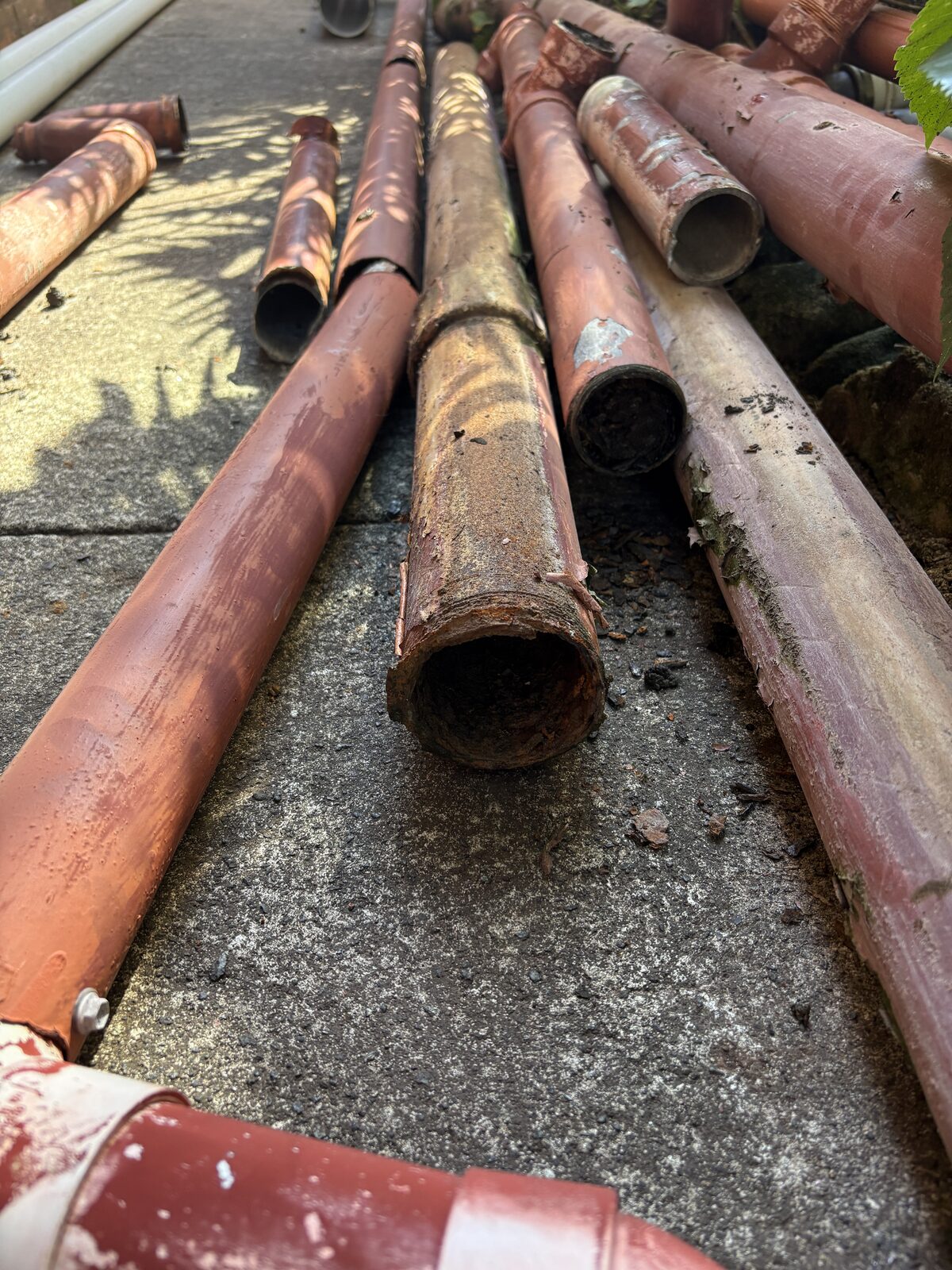 Sections of corroded cast iron waste stack removed from a Coogee strata block, laid out on the paving with rust and scale visible inside the pipe bores