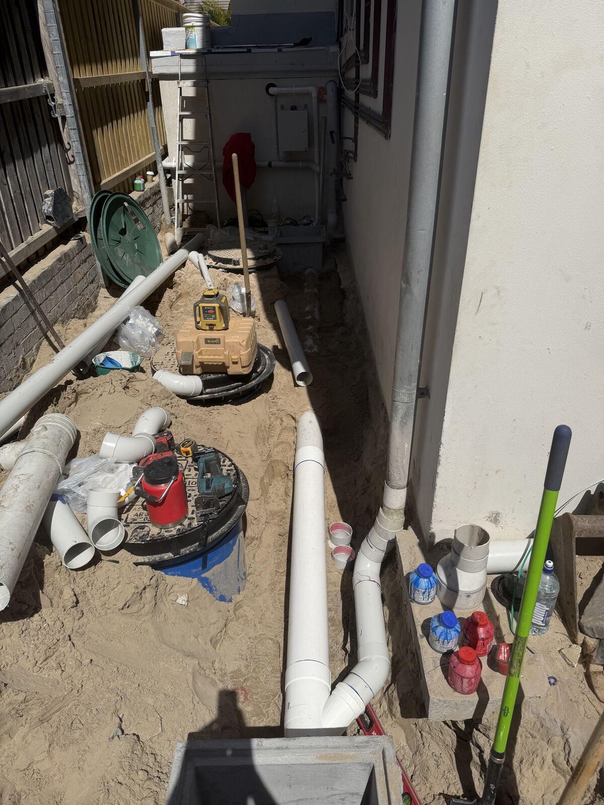 White PVC downpipes connected into a new stormwater line running along the wall of a Bondi home, in a sandy trench