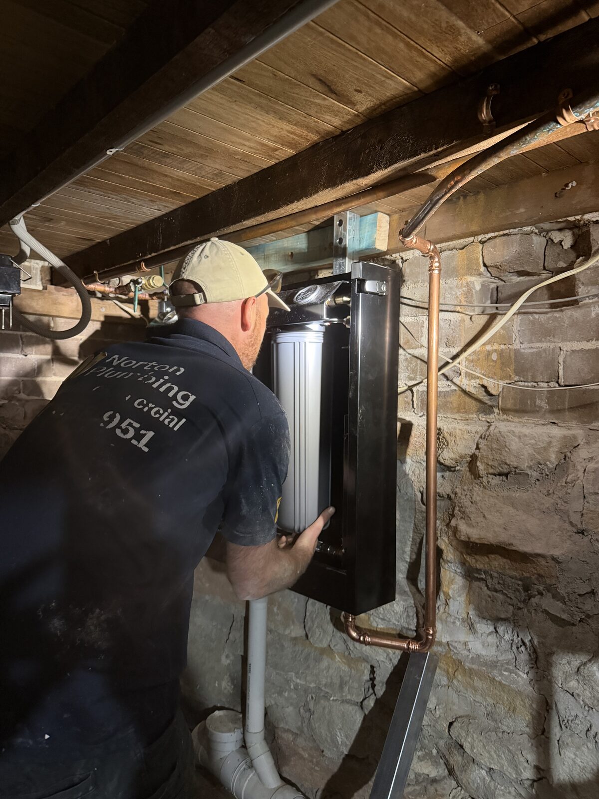 Greg from Norton Plumbing fitting cartridges into an open Puretec FilterWall cabinet on the sandstone basement wall of a North Bondi house