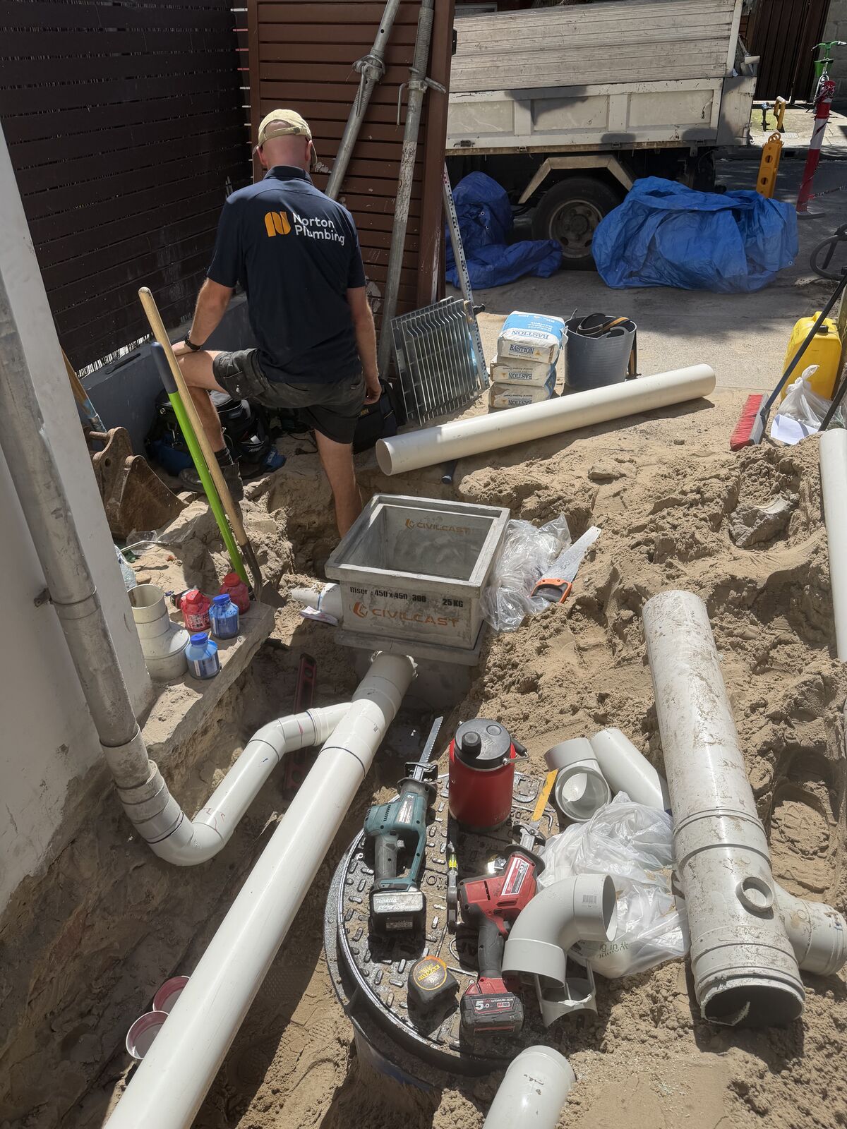 Greg from Norton Plumbing in a dug-out side passage at a Bondi home, beside a new stormwater pit and PVC stormwater pipe connected to the downpipes