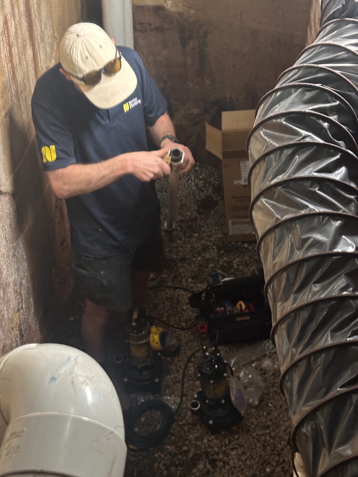 Greg from Norton Plumbing taping the threads on a stainless discharge riser for a replacement rainwater pump in a Dover Heights subfloor