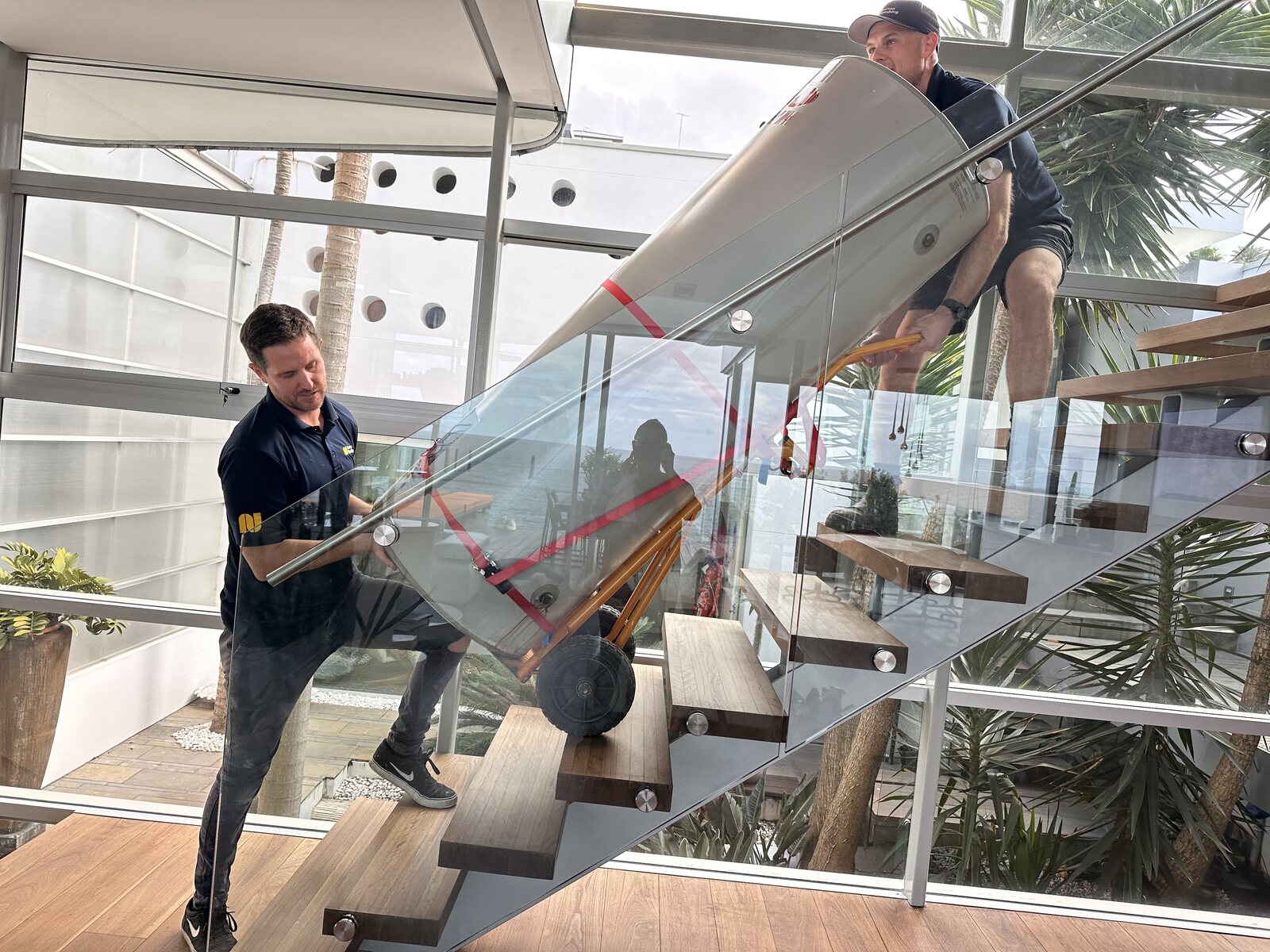 Two Norton Plumbing plumbers carrying a wrapped new hot water cylinder up a staircase during a replacement in Coogee