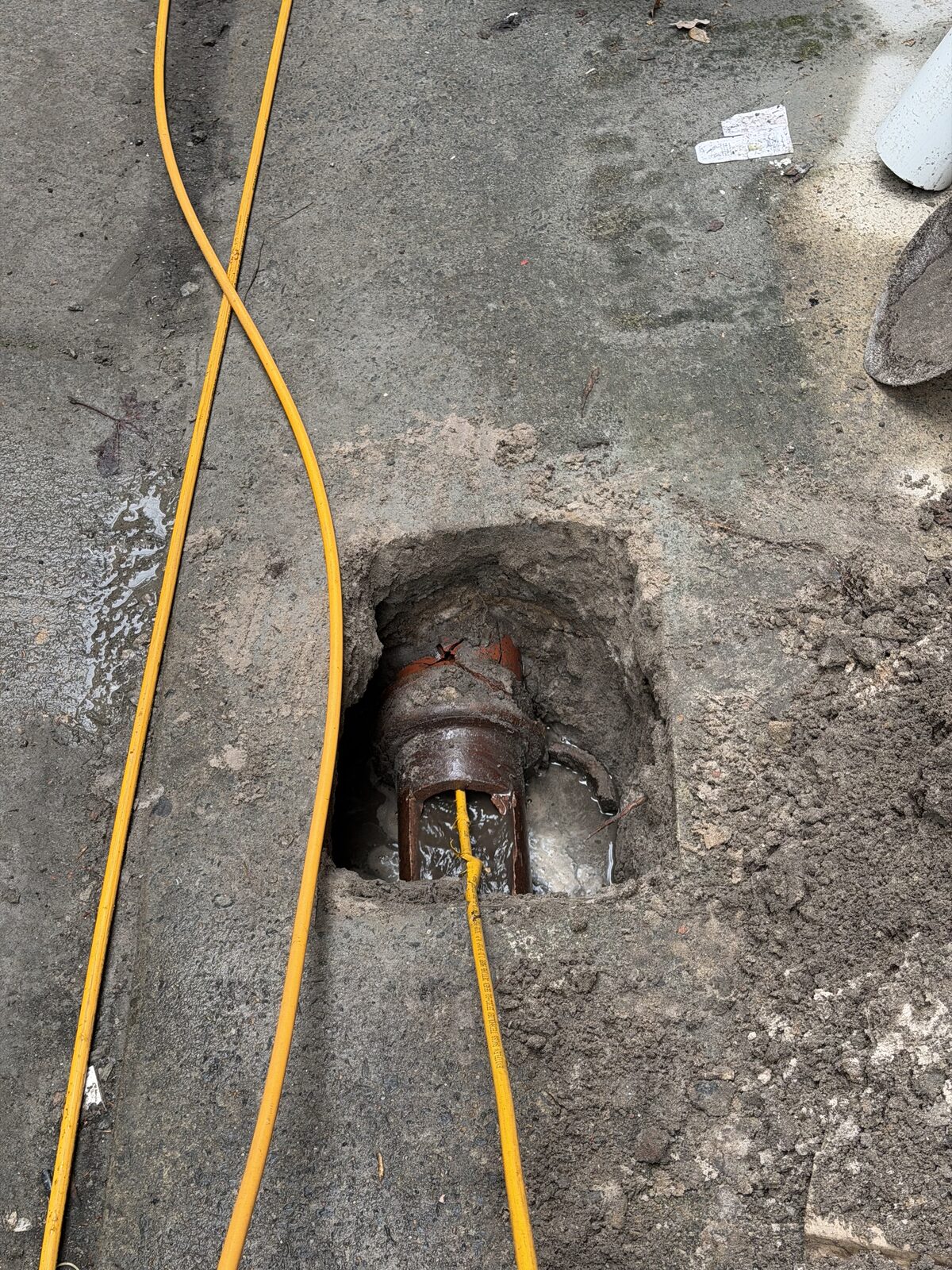 A small square cut in a concrete courtyard in Double Bay exposing an old terracotta stormwater pipe, with a yellow high-pressure jetter hose feeding into the opened line