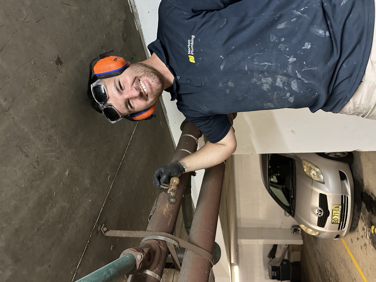 Blake from Norton Plumbing holding the recovered plastic toilet freshener at the drain access point in a Coogee apartment building basement