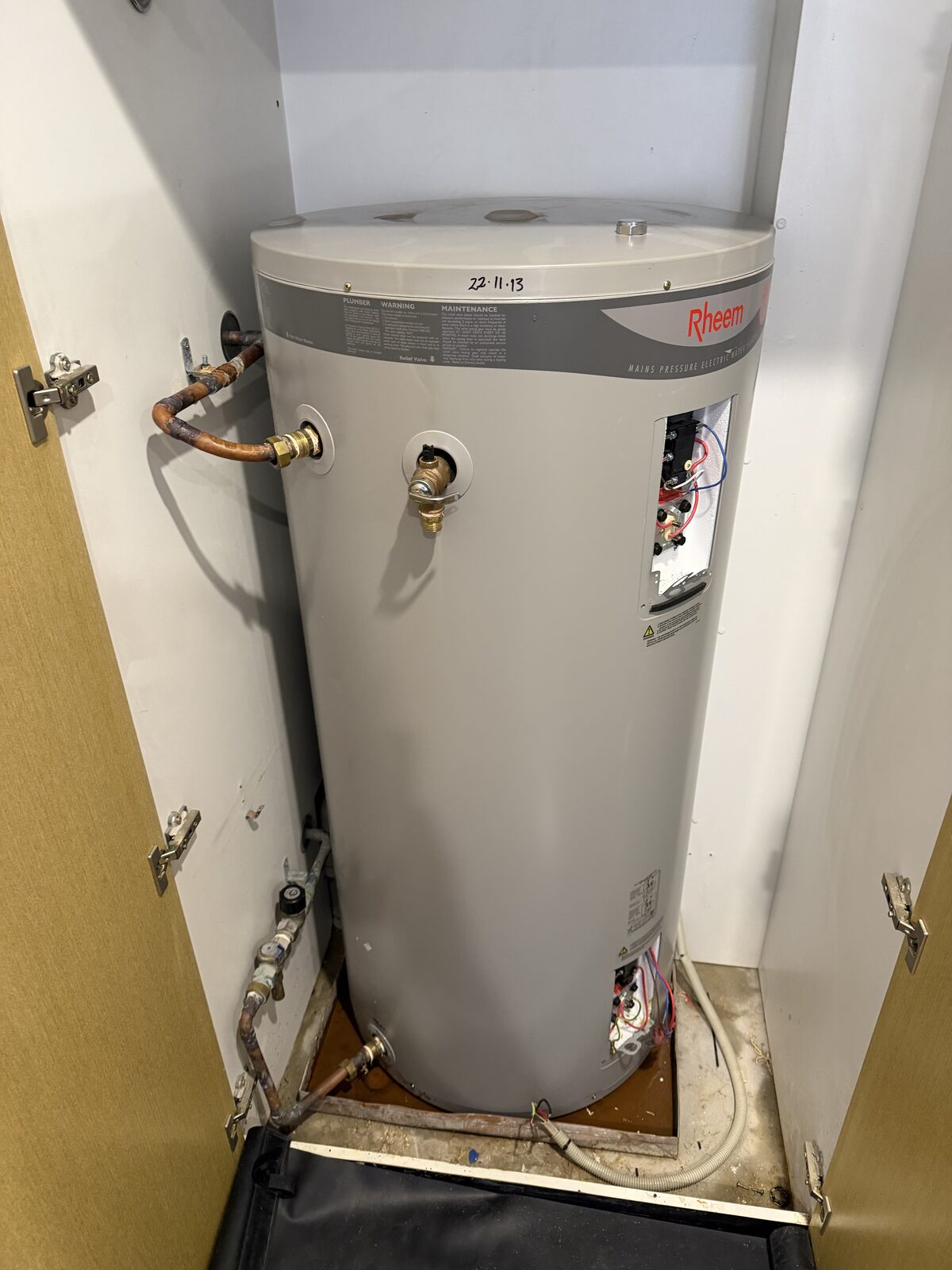 Old Rheem mains pressure electric hot water system in a Darling Point apartment cupboard, with 22.11.13 written on the lid in marker and rust rings on top