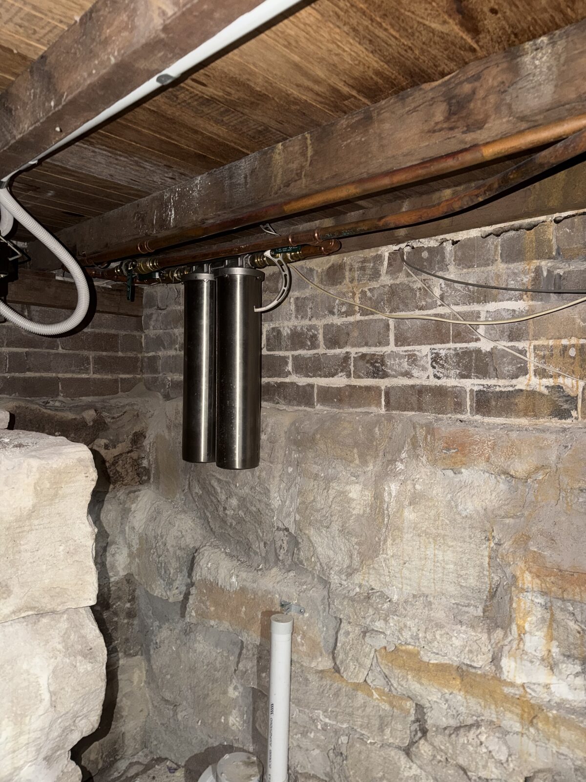 Old twin stainless steel canister water filter plumbed into copper pipework under a North Bondi house, before replacement