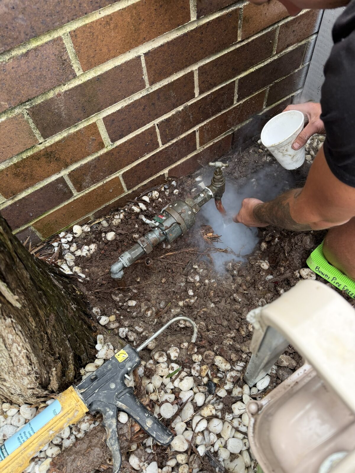 Norton Plumbing plumber working at the frozen copper riser of a water meter in Maroubra while the freezing kit fogs around the pipe