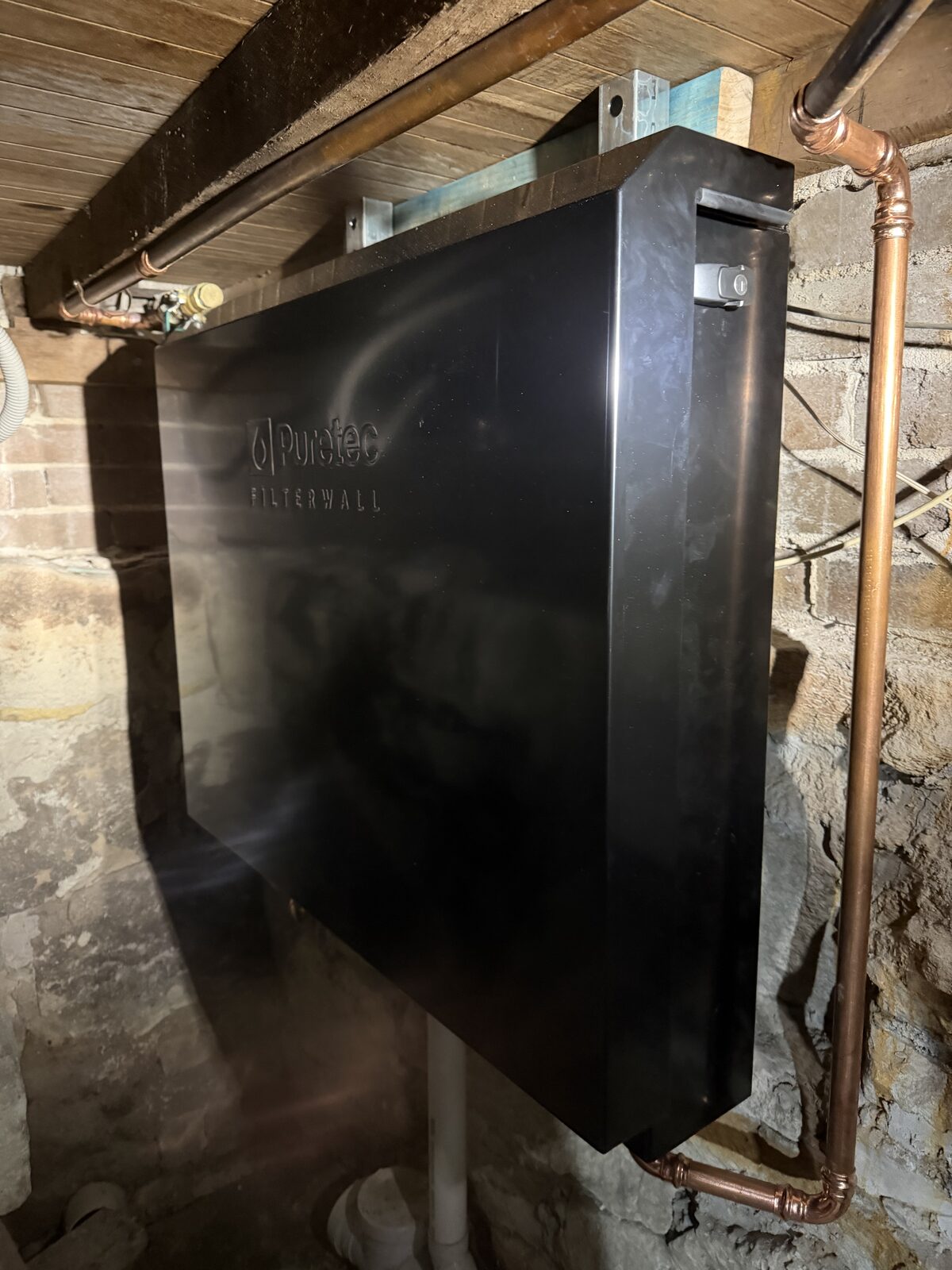 Finished Puretec FilterWall whole-house water filter mounted on the sandstone basement wall under a North Bondi house, with new copper pipework running in and out