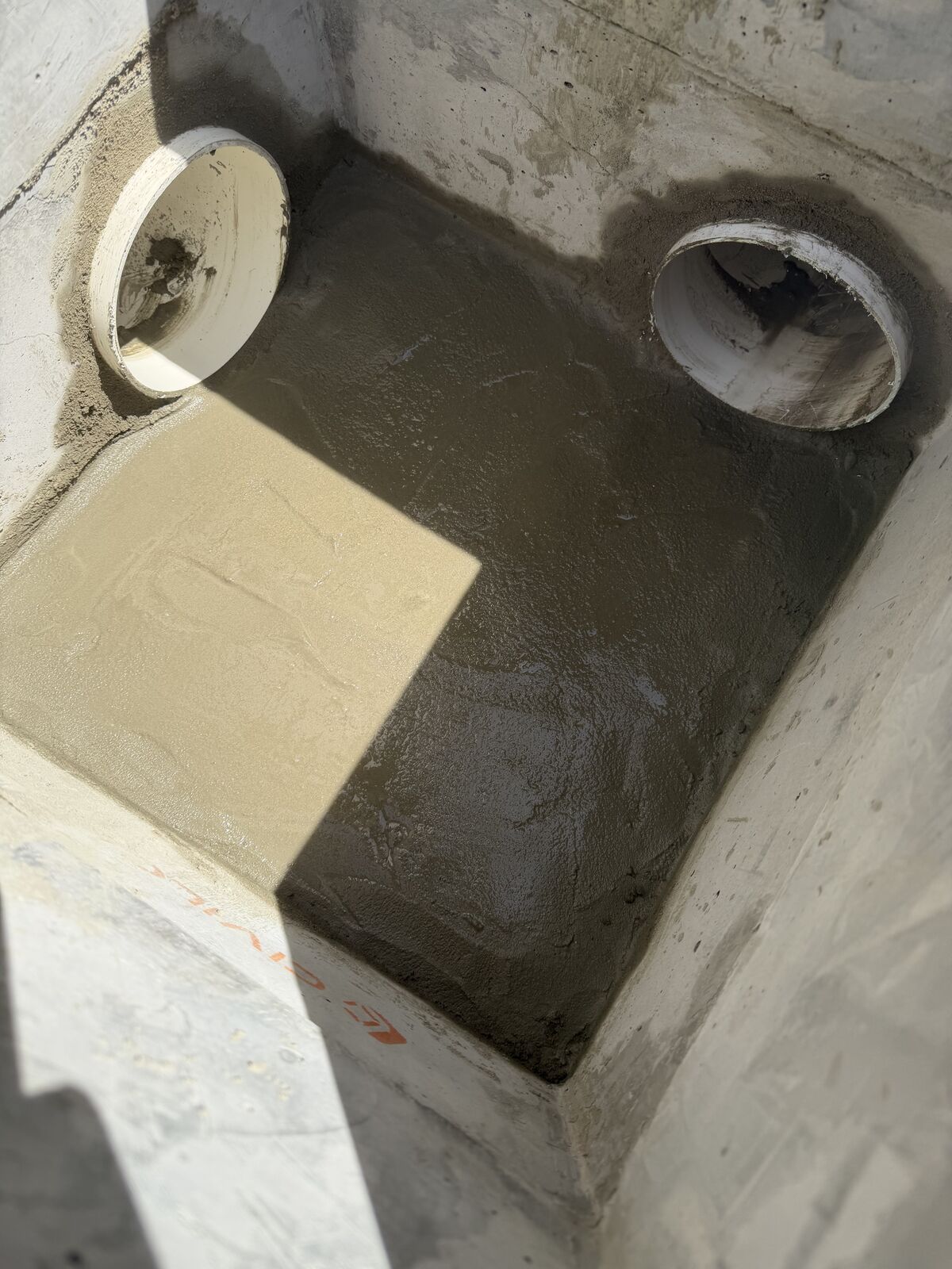 Inside a finished concrete stormwater pit in Bondi, with two pipe connections mortared into the walls and a smooth rendered base
