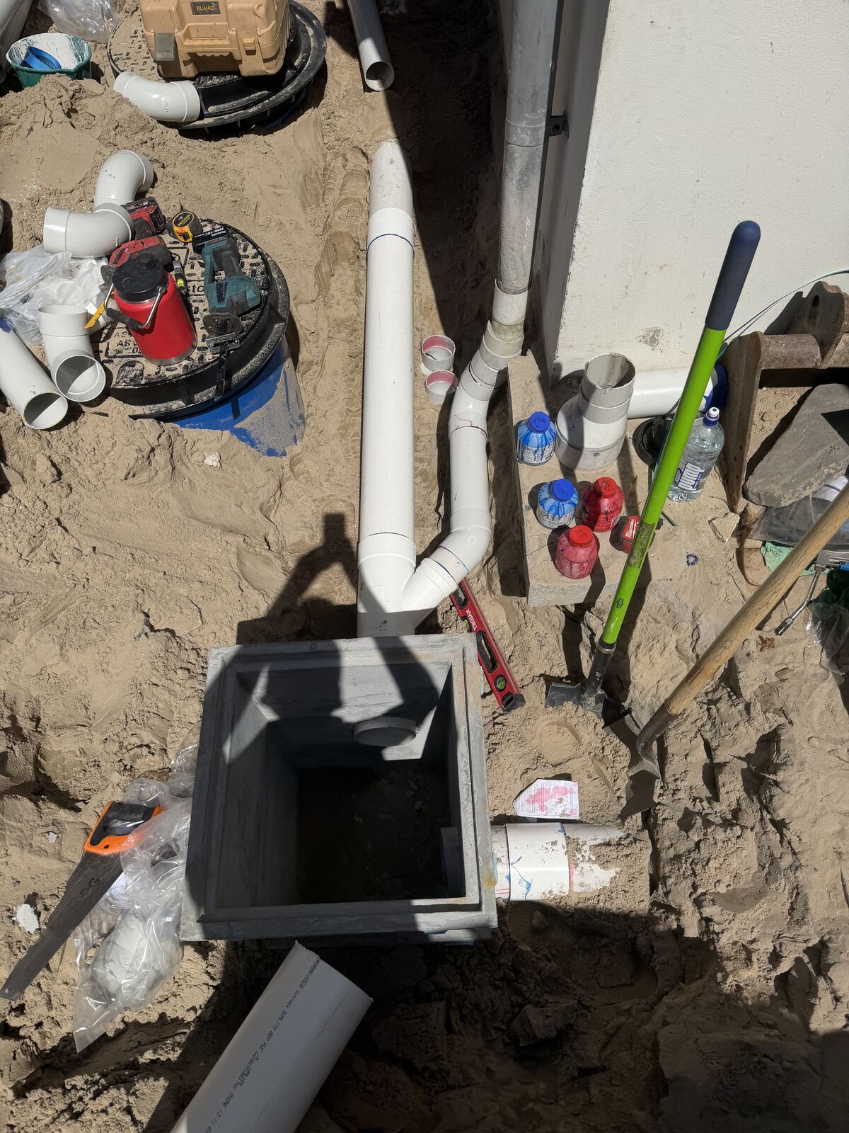 A new square stormwater pit set into sand at the low point of a side passage in Bondi, with the downpipe and PVC stormwater line running towards it