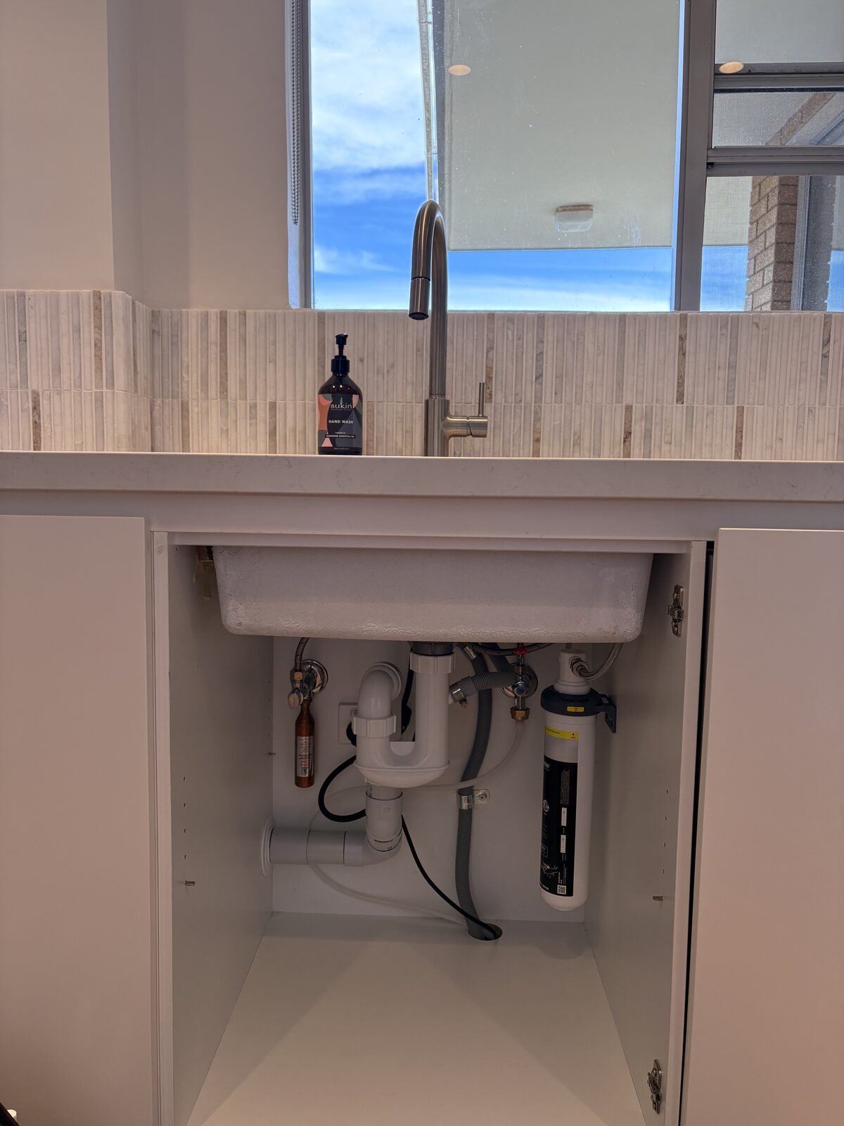 The same Coogee kitchen sink cupboard after installation, showing the Puretec PureMix Z7 under-sink water filter mounted vertically against the cabinet wall clear of the trap and waste